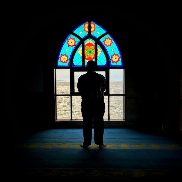 Rear view of silhouette man standing by colorful window in building