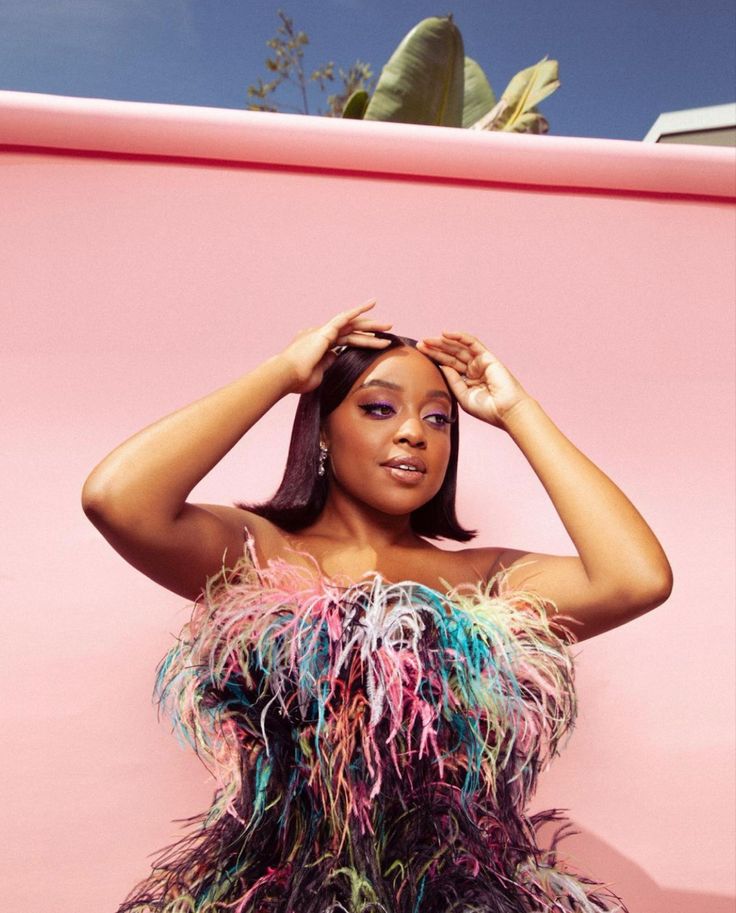 This may contain: a woman in a colorful feathered dress poses for a photo with her hands on her head