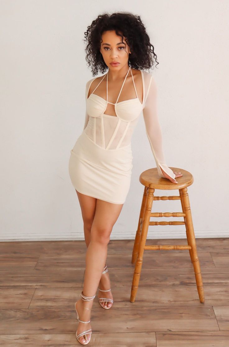 This may contain: a woman in a short white dress leaning on a stool with her legs spread out